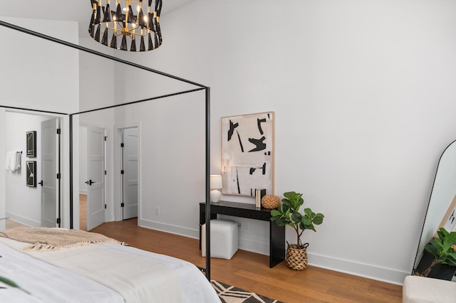 bedroom featuring an inviting chandelier, a high ceiling, baseboards, and wood finished floors