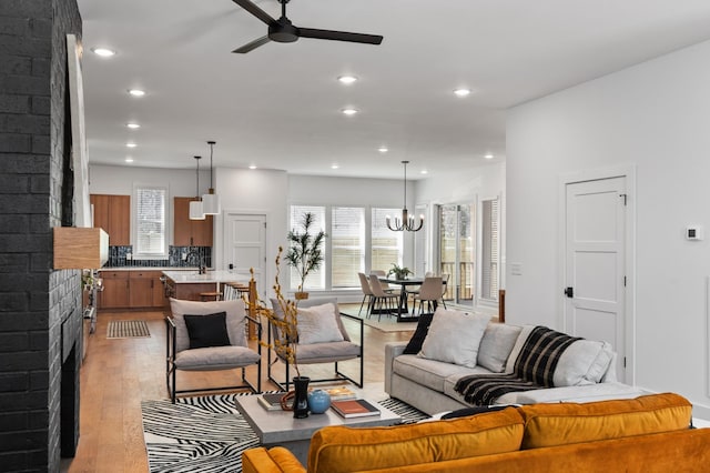 living room with recessed lighting, a fireplace, light wood-style flooring, and ceiling fan with notable chandelier