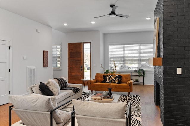 living room featuring a brick fireplace, visible vents, ceiling fan, and wood finished floors