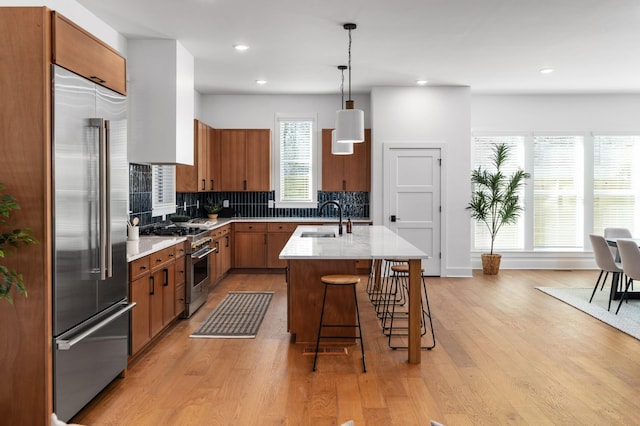 kitchen featuring high end appliances, light wood-type flooring, brown cabinets, and a sink