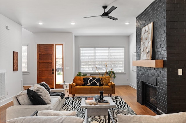 living area with a healthy amount of sunlight, a brick fireplace, light wood-style flooring, and baseboards