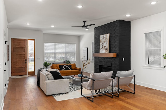 living area with ceiling fan, recessed lighting, baseboards, a brick fireplace, and light wood finished floors