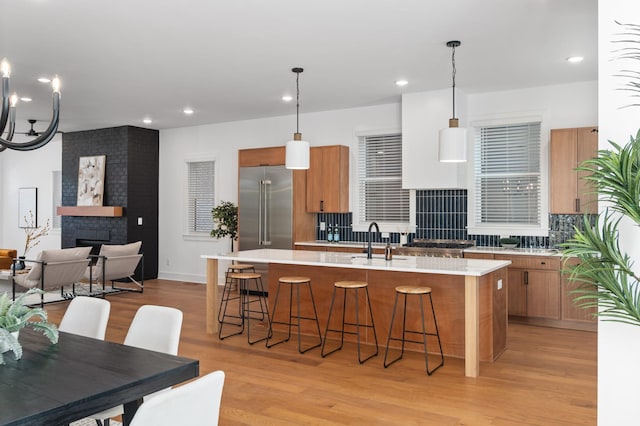 kitchen featuring a fireplace, light countertops, light wood-style floors, a kitchen island with sink, and built in refrigerator