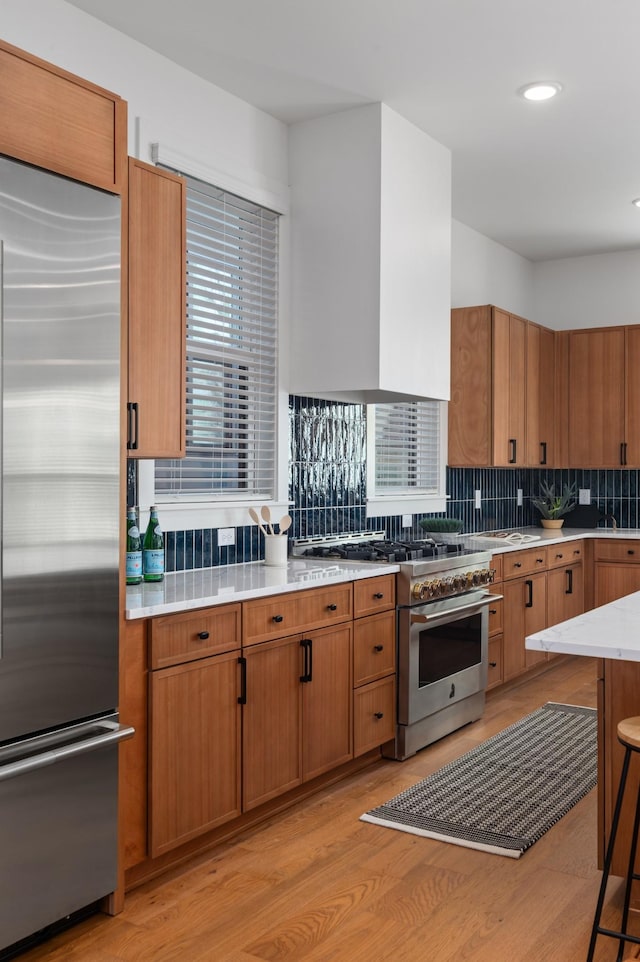 kitchen with light wood-type flooring, tasteful backsplash, high quality appliances, and brown cabinetry