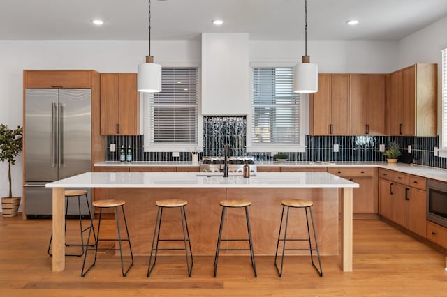 kitchen featuring built in appliances, light wood-style flooring, a sink, light countertops, and tasteful backsplash