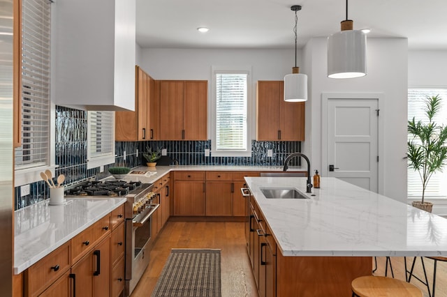 kitchen with an island with sink, brown cabinets, high end stainless steel range oven, light wood-style floors, and a sink