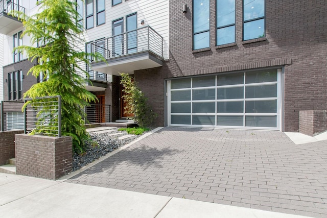 entrance to property with a balcony, a garage, decorative driveway, and brick siding