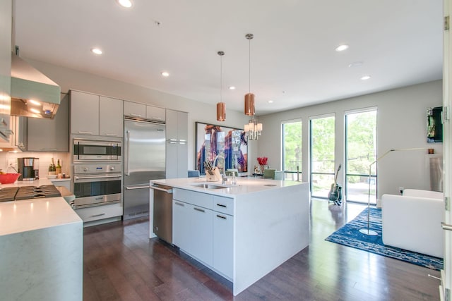 kitchen with wall chimney exhaust hood, dark wood-style flooring, built in appliances, light countertops, and a sink