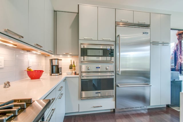 kitchen featuring tasteful backsplash, light countertops, dark wood finished floors, and built in appliances