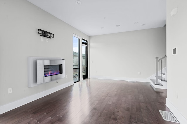 unfurnished living room featuring a glass covered fireplace, dark wood-style flooring, visible vents, and stairs