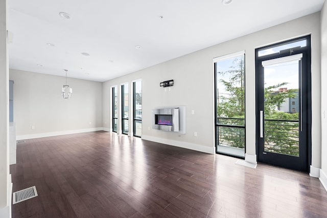 unfurnished living room with dark wood-type flooring, a glass covered fireplace, baseboards, and recessed lighting