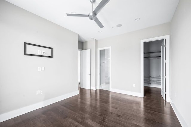 unfurnished bedroom with baseboards, ensuite bath, wood finished floors, a walk in closet, and a closet