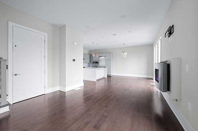 unfurnished living room with dark wood-style floors, a glass covered fireplace, baseboards, and recessed lighting