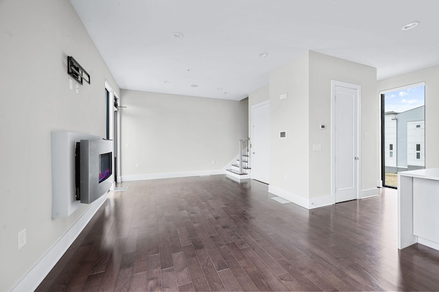 unfurnished living room with baseboards, a glass covered fireplace, stairway, dark wood-style flooring, and recessed lighting