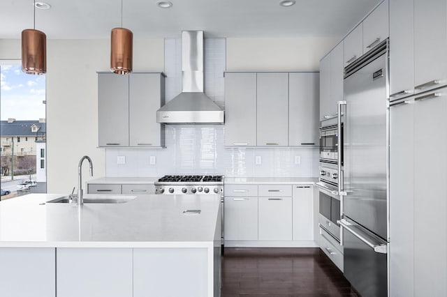 kitchen featuring stainless steel appliances, a sink, wall chimney range hood, decorative backsplash, and dark wood finished floors