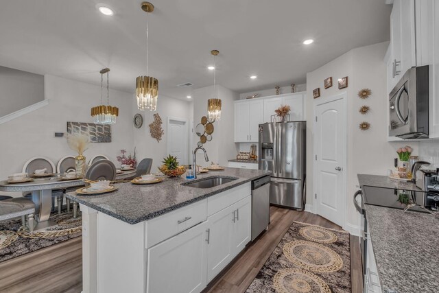 kitchen featuring white cabinets, an island with sink, dark wood-style flooring, stainless steel appliances, and a sink