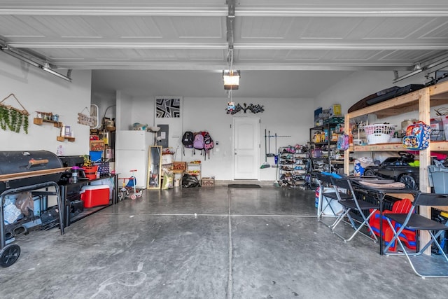 garage featuring a garage door opener, freestanding refrigerator, electric panel, and a workshop area