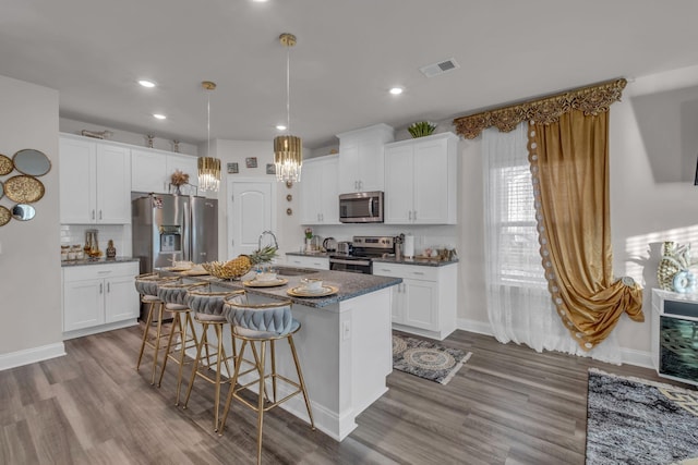 kitchen featuring visible vents, appliances with stainless steel finishes, a kitchen island with sink, a sink, and a kitchen breakfast bar