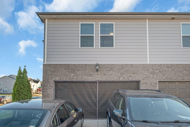 view of side of property with driveway, brick siding, and an attached garage