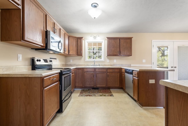 kitchen with brown cabinetry, appliances with stainless steel finishes, a peninsula, light countertops, and a sink