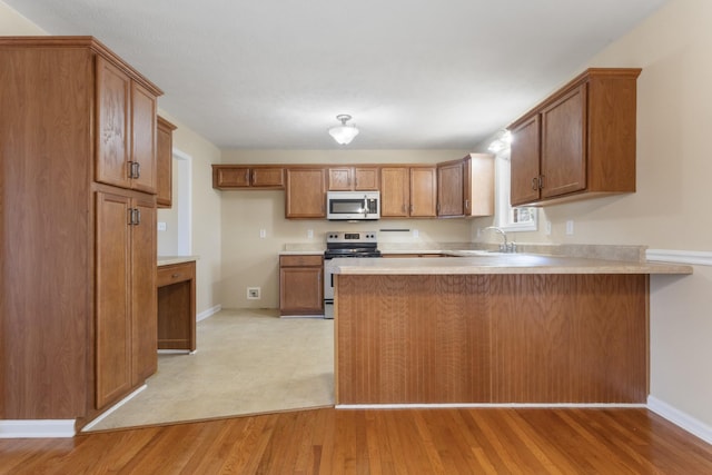 kitchen featuring brown cabinetry, appliances with stainless steel finishes, a peninsula, light countertops, and light wood-style floors