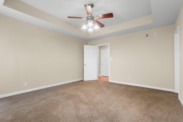 empty room with carpet floors, a tray ceiling, ceiling fan, and baseboards