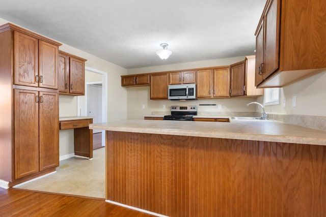 kitchen featuring a peninsula, a sink, light countertops, appliances with stainless steel finishes, and brown cabinets