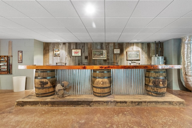 bar featuring concrete flooring, concrete block wall, gas water heater, and a drop ceiling