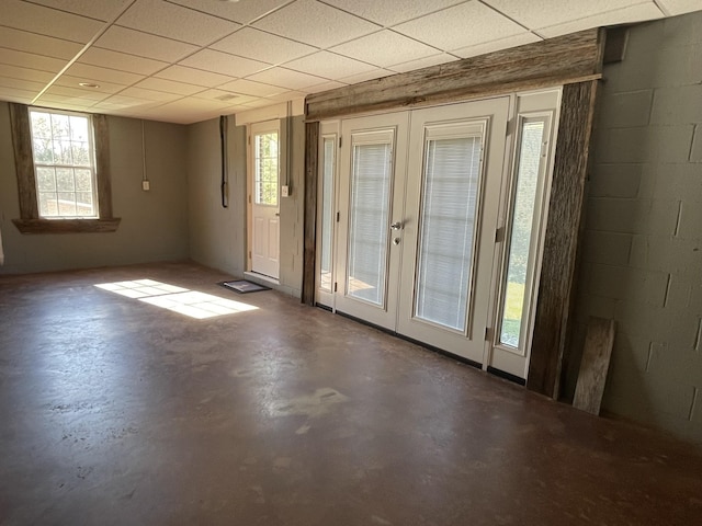 interior space with concrete block wall, concrete floors, a drop ceiling, and french doors