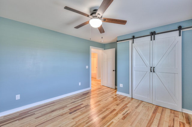 unfurnished bedroom with a barn door, baseboards, and light wood-style flooring