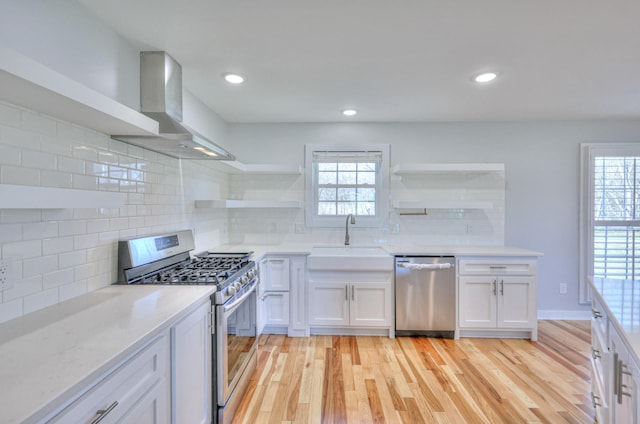 kitchen featuring appliances with stainless steel finishes, a healthy amount of sunlight, wall chimney range hood, open shelves, and a sink