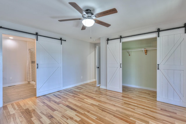 unfurnished bedroom with light wood-style floors, baseboards, and a barn door