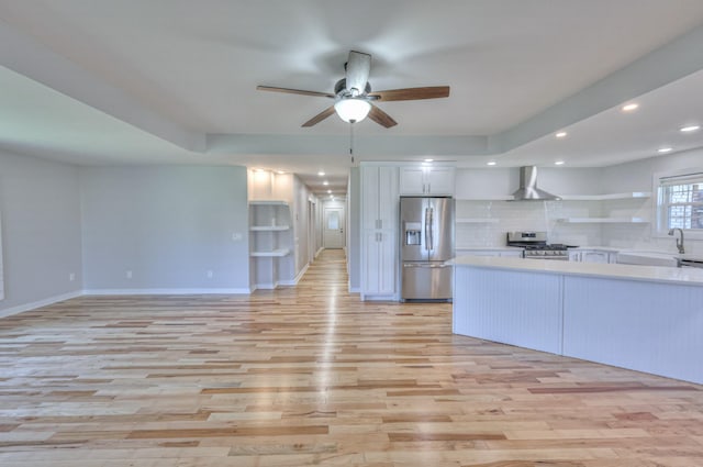 kitchen featuring open shelves, light countertops, light wood-style flooring, appliances with stainless steel finishes, and wall chimney range hood