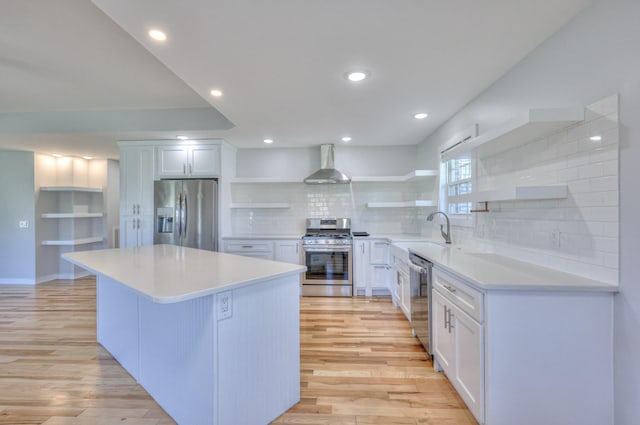 kitchen featuring light wood-style flooring, a sink, appliances with stainless steel finishes, wall chimney range hood, and open shelves