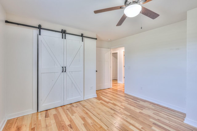 unfurnished bedroom featuring a barn door, wood finished floors, a ceiling fan, and baseboards