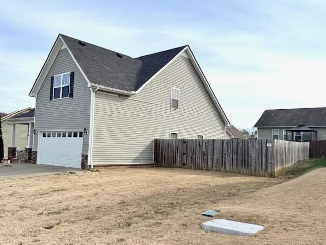 view of property exterior featuring an attached garage, fence, and driveway