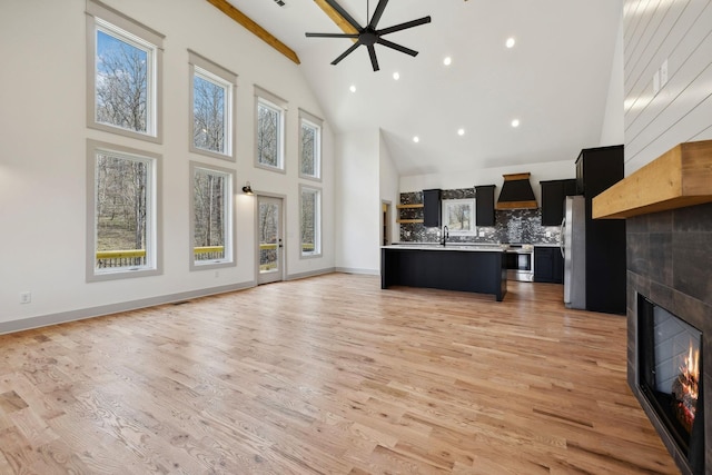 unfurnished living room with baseboards, high vaulted ceiling, a tiled fireplace, and light wood-style floors