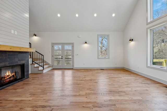 unfurnished living room with light wood-type flooring, a fireplace, high vaulted ceiling, and french doors