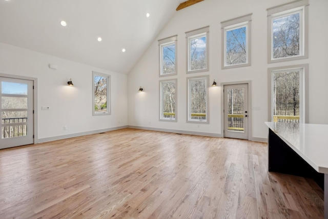 unfurnished living room featuring high vaulted ceiling, plenty of natural light, and light wood-style floors