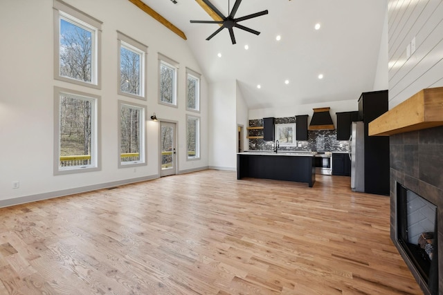 unfurnished living room with light wood-type flooring, baseboards, high vaulted ceiling, and a tile fireplace