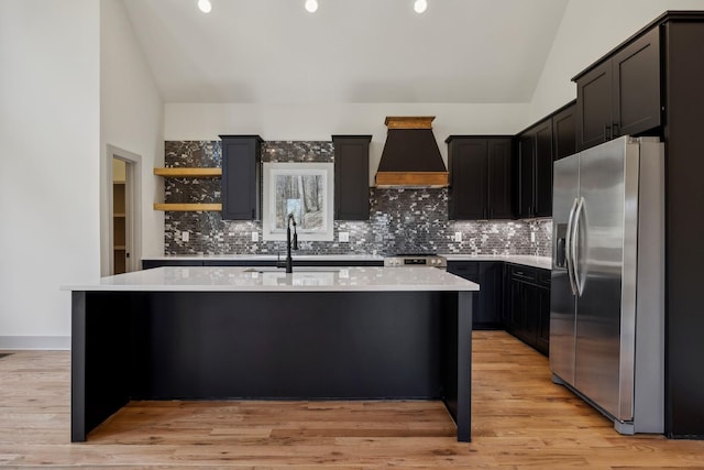 kitchen featuring lofted ceiling, a kitchen island with sink, stainless steel appliances, light countertops, and custom exhaust hood