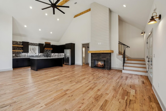 kitchen with a tiled fireplace, open floor plan, dark cabinets, light wood-style floors, and stainless steel refrigerator with ice dispenser