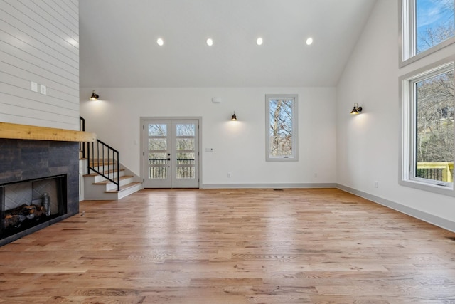 unfurnished living room with high vaulted ceiling, french doors, light wood-style flooring, and a tiled fireplace