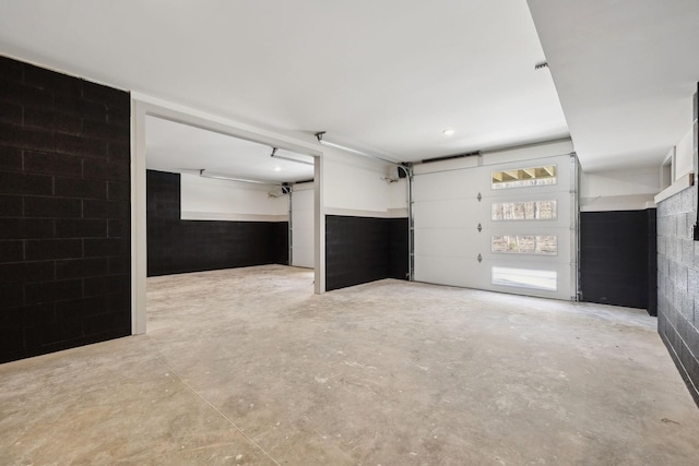 unfurnished living room featuring a garage, concrete block wall, and concrete flooring