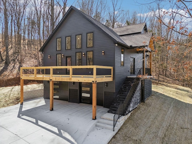 exterior space with a deck, a garage, a shingled roof, stairs, and concrete driveway