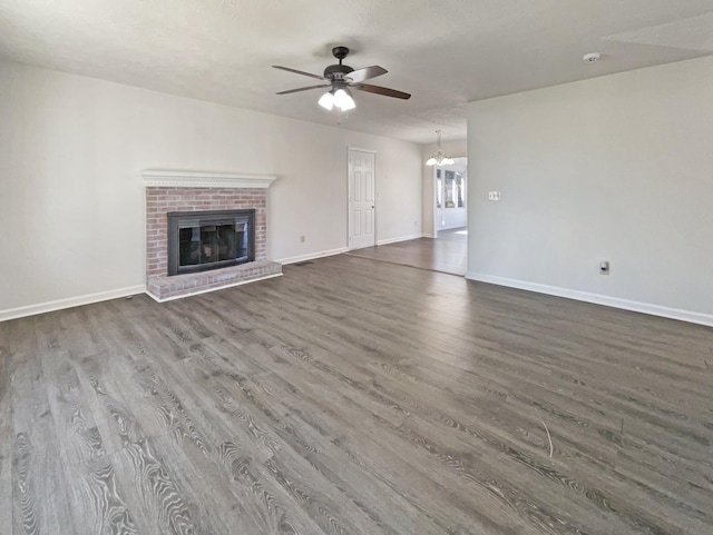 unfurnished living room featuring a brick fireplace, baseboards, dark wood finished floors, and ceiling fan with notable chandelier