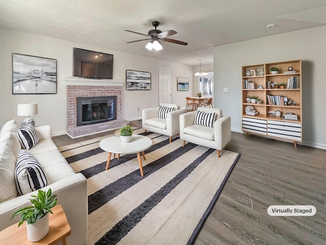 living area with ceiling fan with notable chandelier, a brick fireplace, wood finished floors, and baseboards