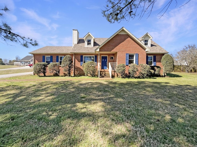 new england style home featuring brick siding, a front lawn, a chimney, and a shingled roof