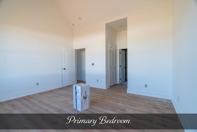 spare room featuring high vaulted ceiling, wood finished floors, and baseboards