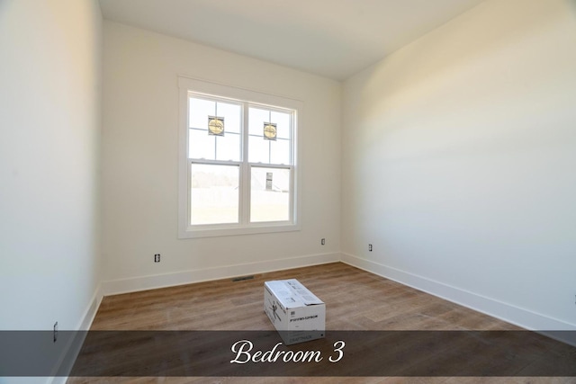 empty room featuring wood finished floors, visible vents, and baseboards